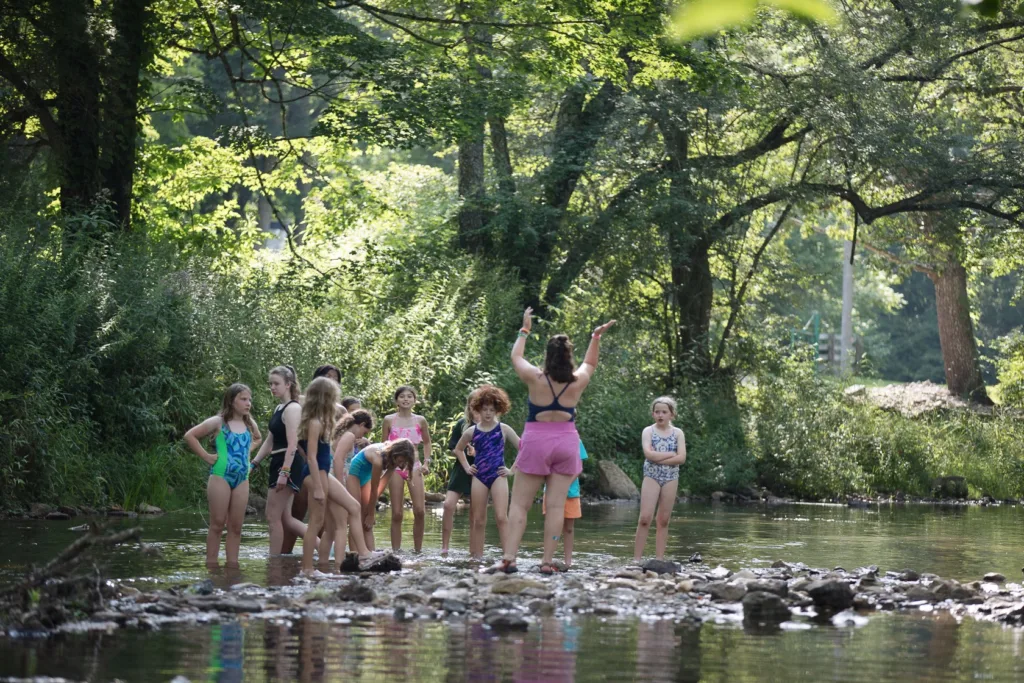 Campers listen to a counselor in a shallow portion of the creek