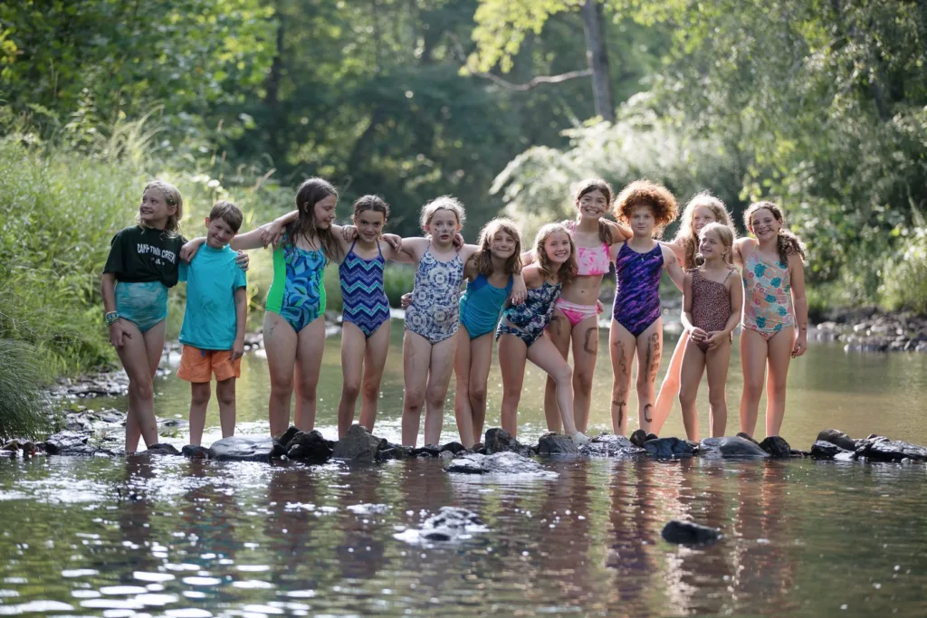 A group of campers stand smiling arm in arm in a shallow portion of the creek