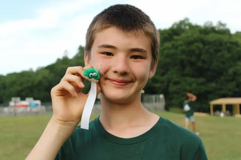 a camper holds a small "fuzzie" camp award next to his face