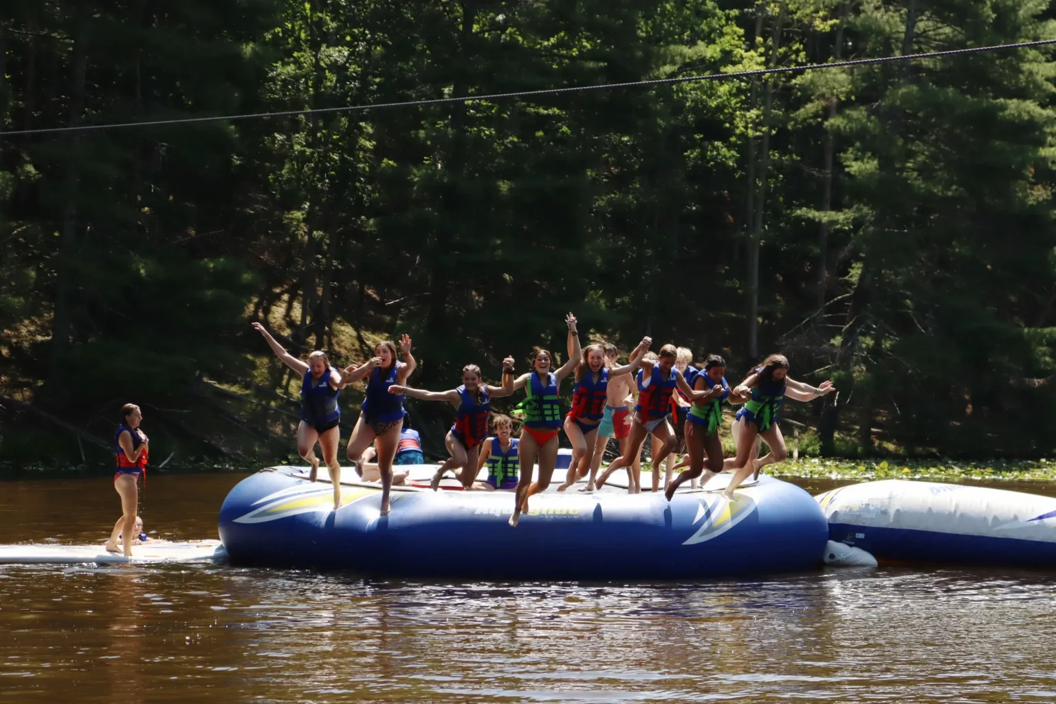 Campers at Camp Twin Creeks jump in the creek together hand in hand