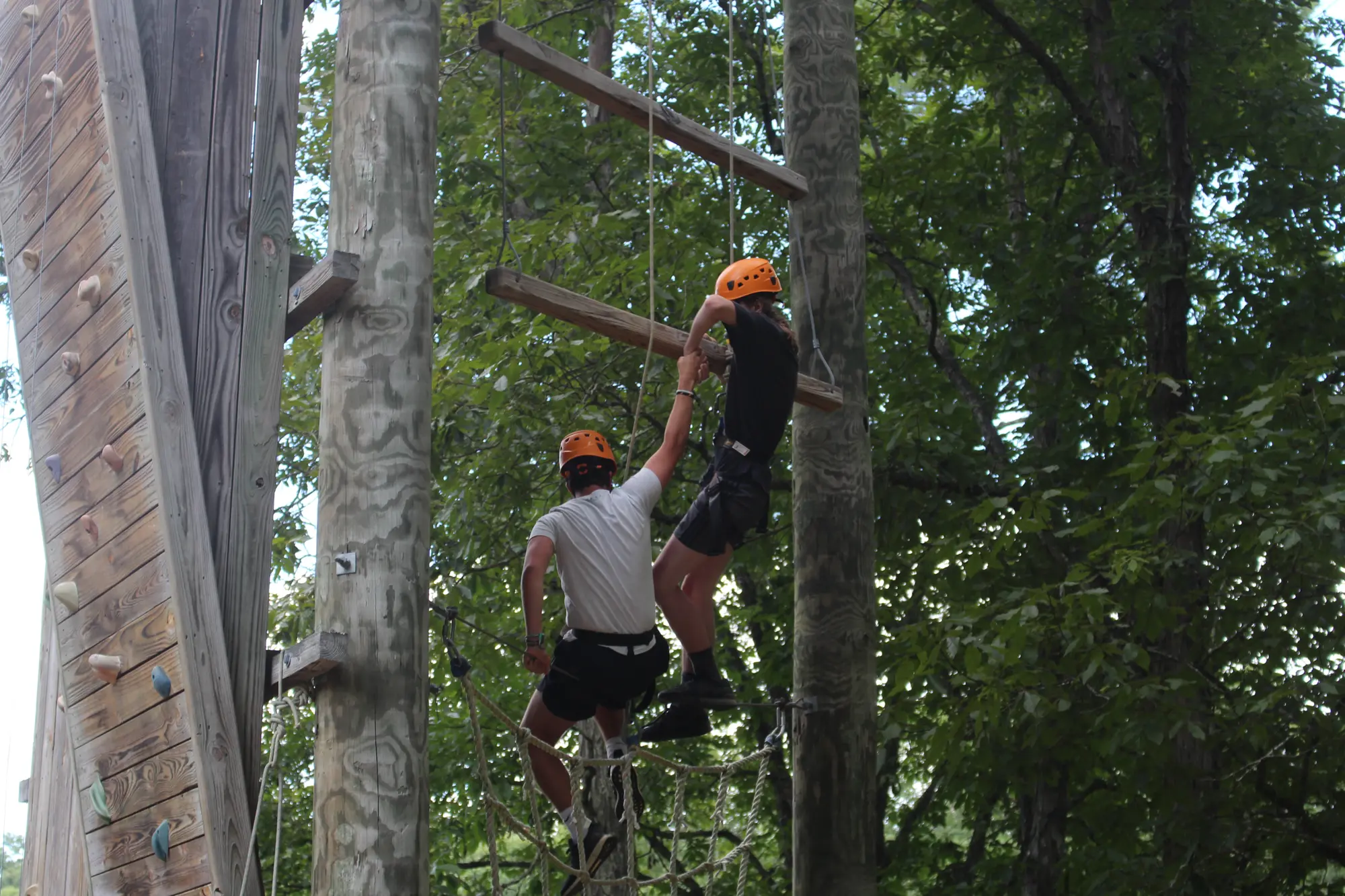 a camper helps another camper up a climbing wall